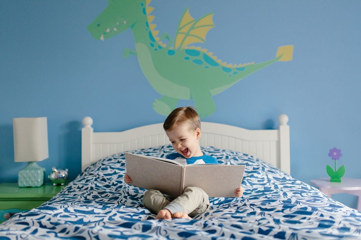 https://www.kindercare.com/-/media/contenthub/images/article-images/activities-for-kids/books-galore/oh-wonder-10-delightful-books-to-power-up-your-childs-imagination/feature-image_happy-boy-reading-in-bedroom-dragon-on-wall.jpg